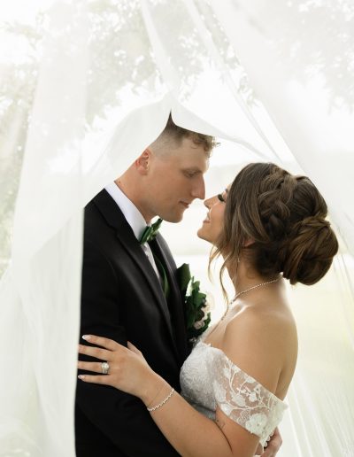 Bride and groom under the veil showcasing a braided bridal updo by Milk + Honey The Hair Lounge in Cary, NC