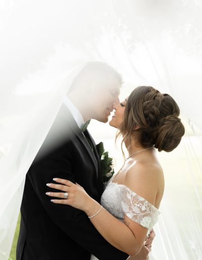 Bride with a braided low-bun updo beneath her veil, wedding hair by Milk + Honey The Hair Lounge in Cary, NC